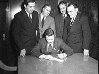 American Red Cross check Four suited males look on as Henry Ford II signs a check for the American Red Cross.